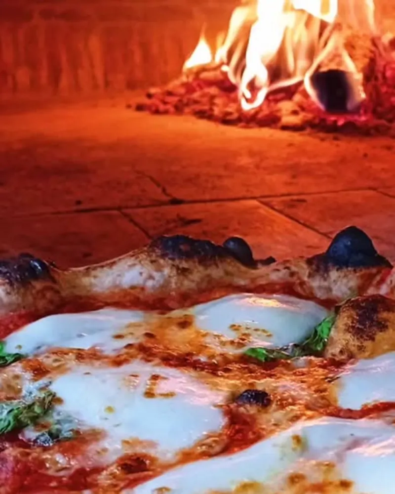 Vue à l'intérieur du four à 450 degrés : flammes au fond, hearth orangé, pizza en pleine cuisson au premier plan