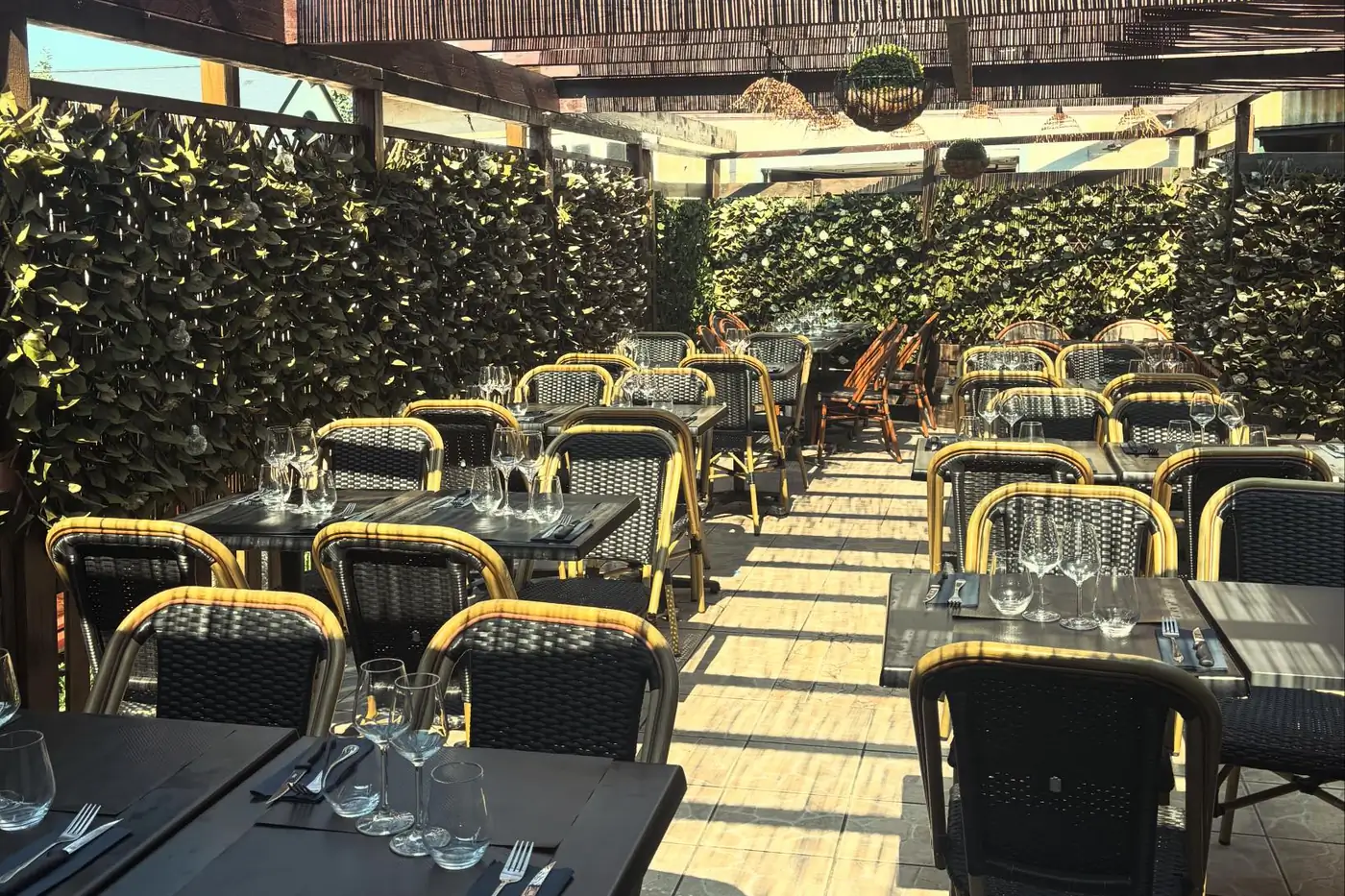 Terrasse extérieure d'Il Piacere avec treillis en bois, chaises rotin et tables alignées en perspective sous la lumière du jour