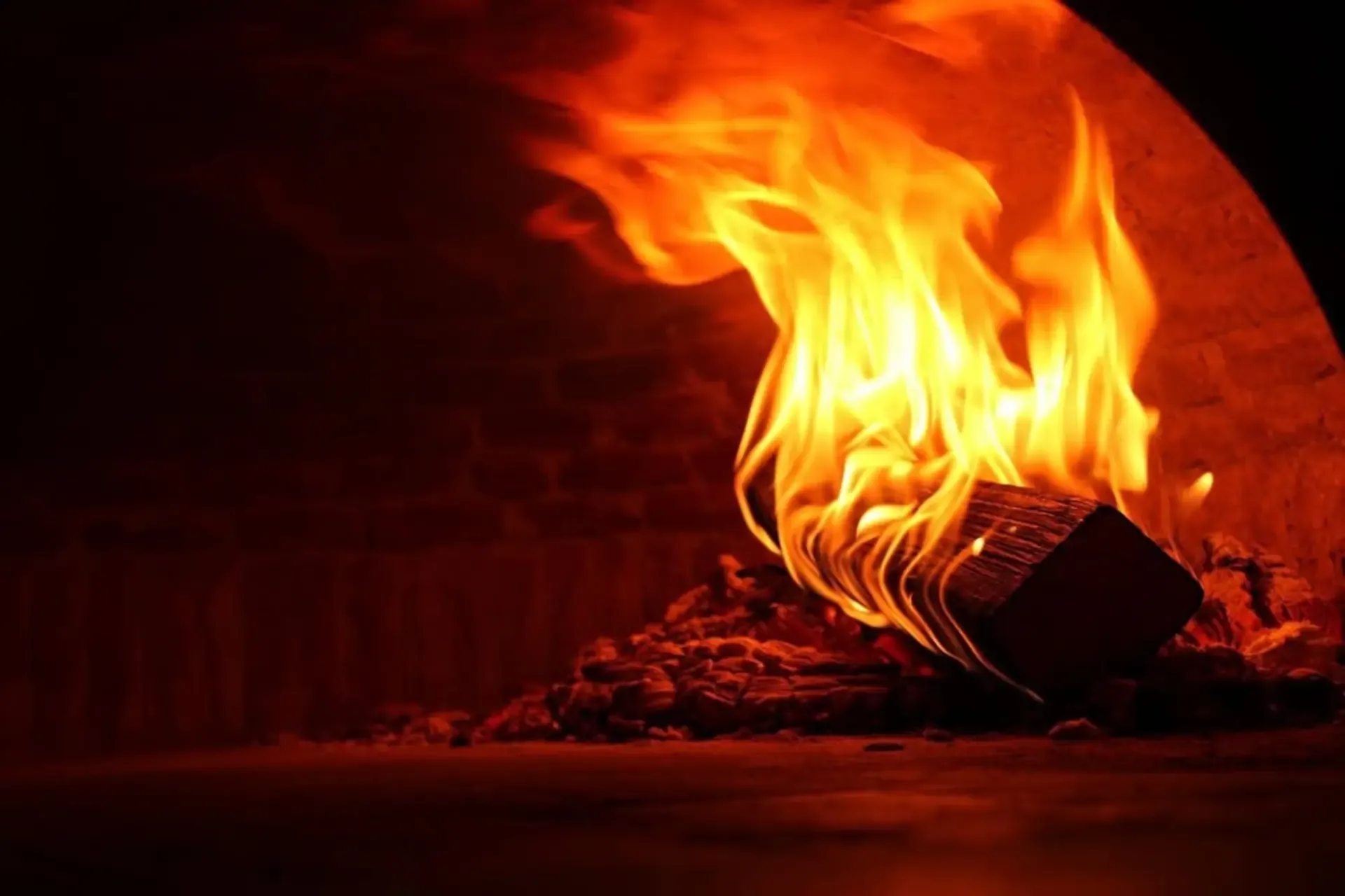 Bûche en flammes dans le four à pizza napolitain d'Il Piacere, ambiance soir, flammes orange jaillissant sur fond noir